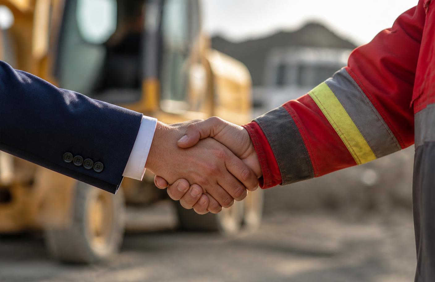 Business partner and site contractor shaking hands in front of yellow machinery